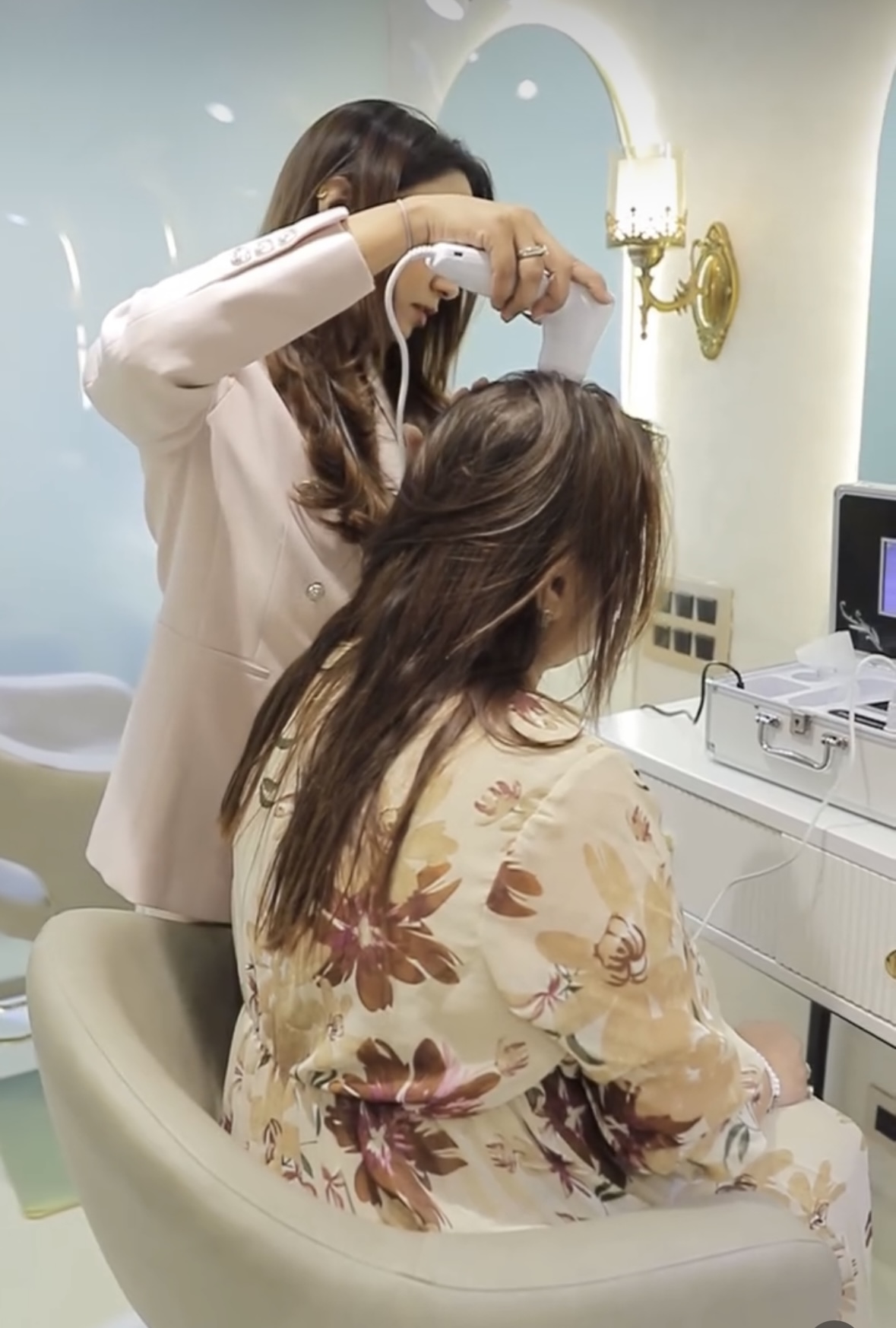 A therapist examining a client's scalp with a handheld device while the client sits in a salon chair